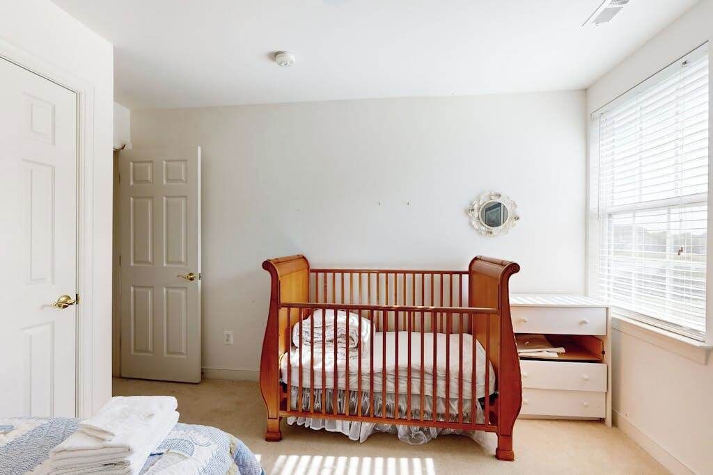 A bedroom with a wooden crib, a white dresser, a mirror on the wall, and a door.