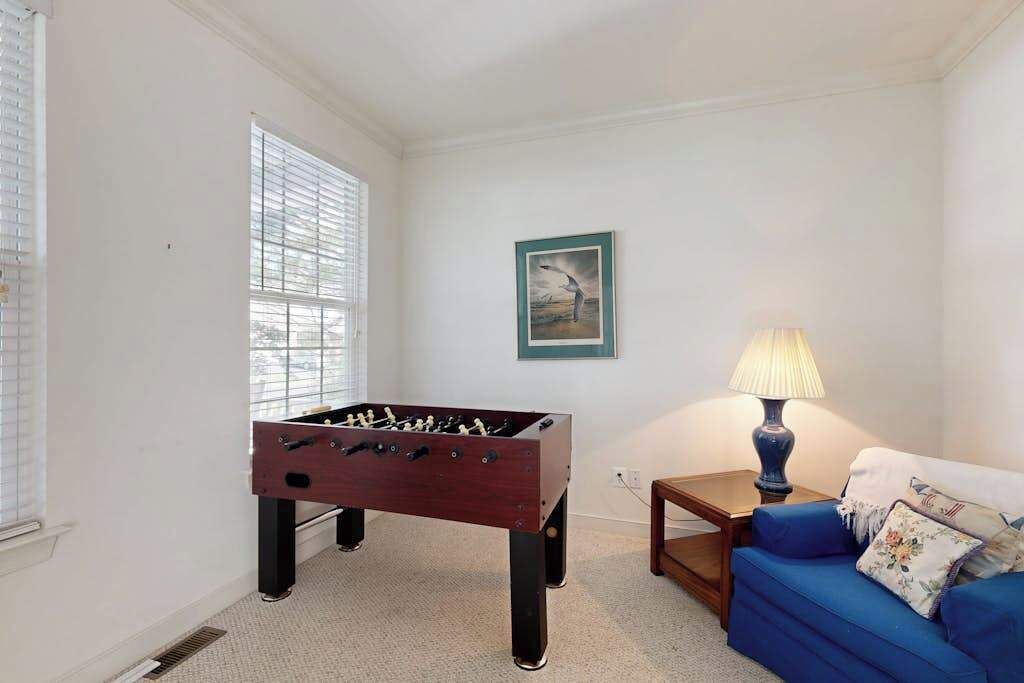A room with a foosball table, a blue sofa, a lamp, and a framed picture on the wall.