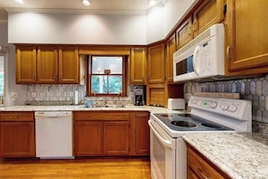 Una cocina con armarios de madera, microondas integrado, estufa y lavavajillas.