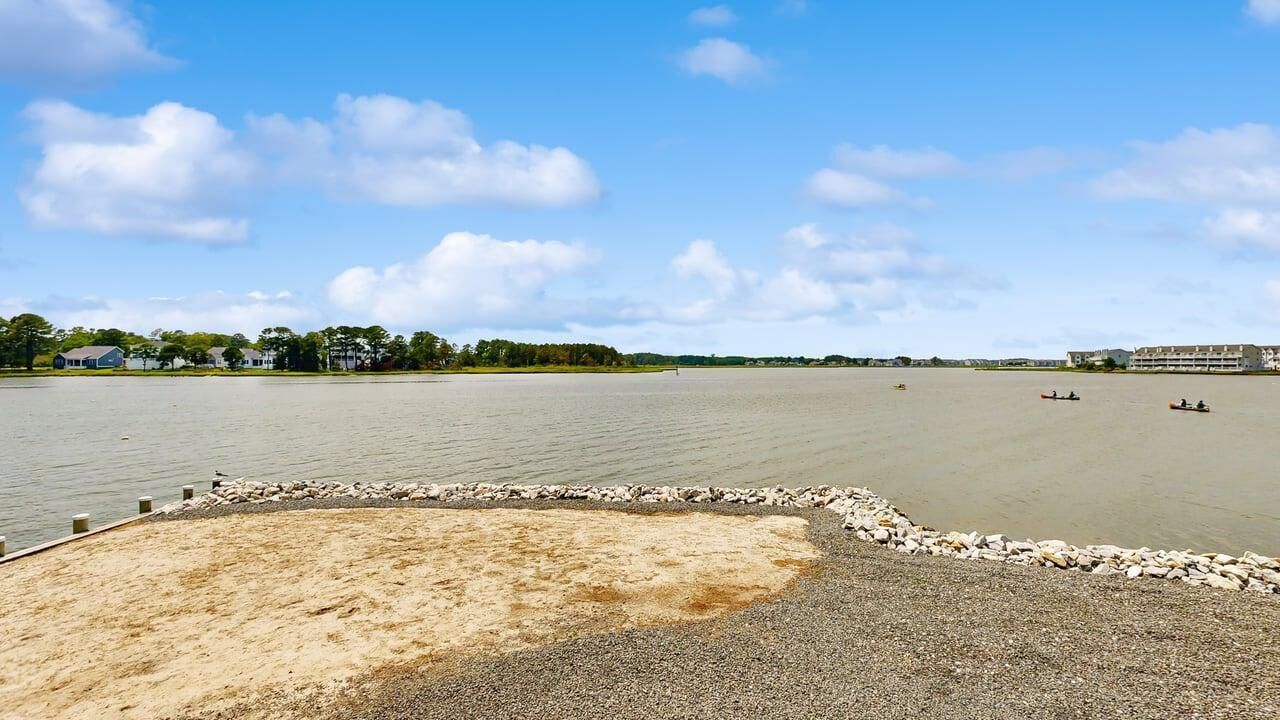 A wide, calm water body with a sandy area in the foreground and buildings in the background.