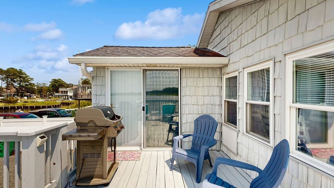 A covered outdoor deck with a grill, two chairs, and a sliding glass door leading to a patio.