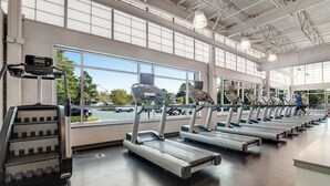 Une salle de sport équipée de plusieurs tapis de course, d’un appareil de marche en escalier et de grandes fenêtres.