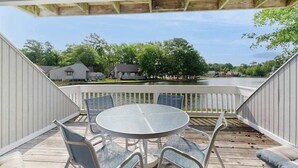Une terrasse extérieure couverte, dotée d’une table ronde et de chaises, qui offre une vue sur un plan d’eau et sur des maisons.