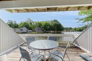 Een overdekt terras buiten met een ronde tafel en stoelen, met uitzicht op een wateroppervlak en huizen.