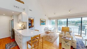 Een moderne keuken met een groot eiland, een eethoek met stoelen, en uitzicht op een meer door grote ramen.