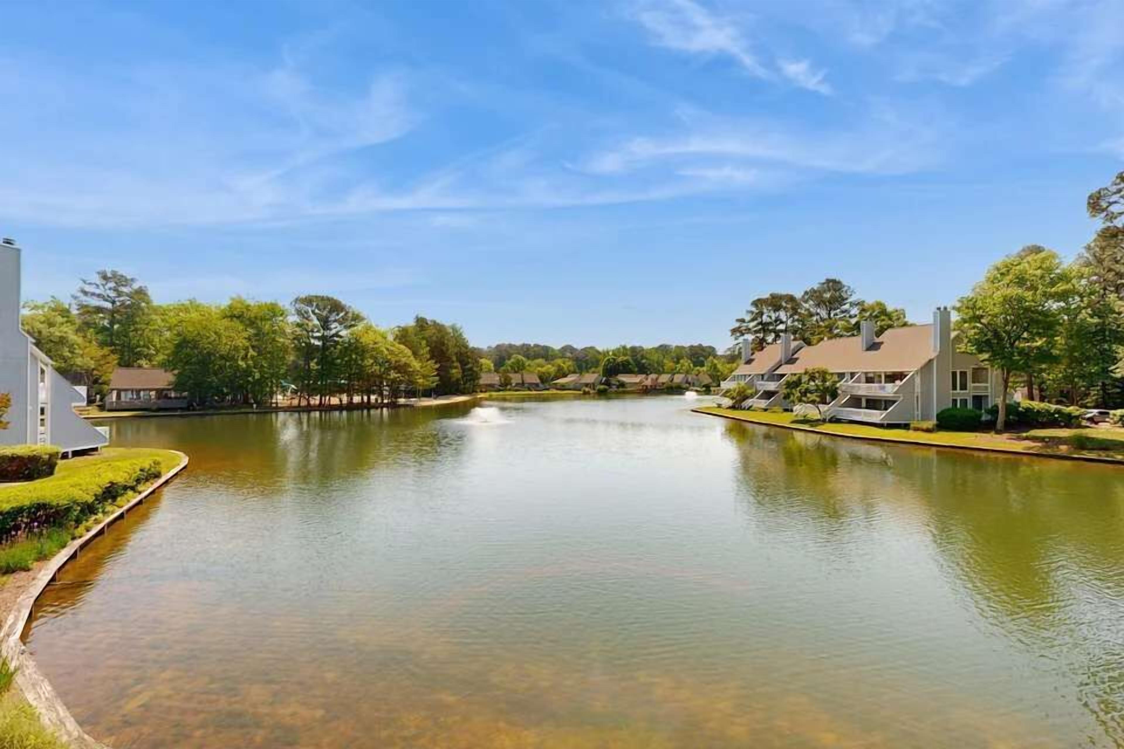 A serene lake with houses on the banks, clear skies, and lush greenery.