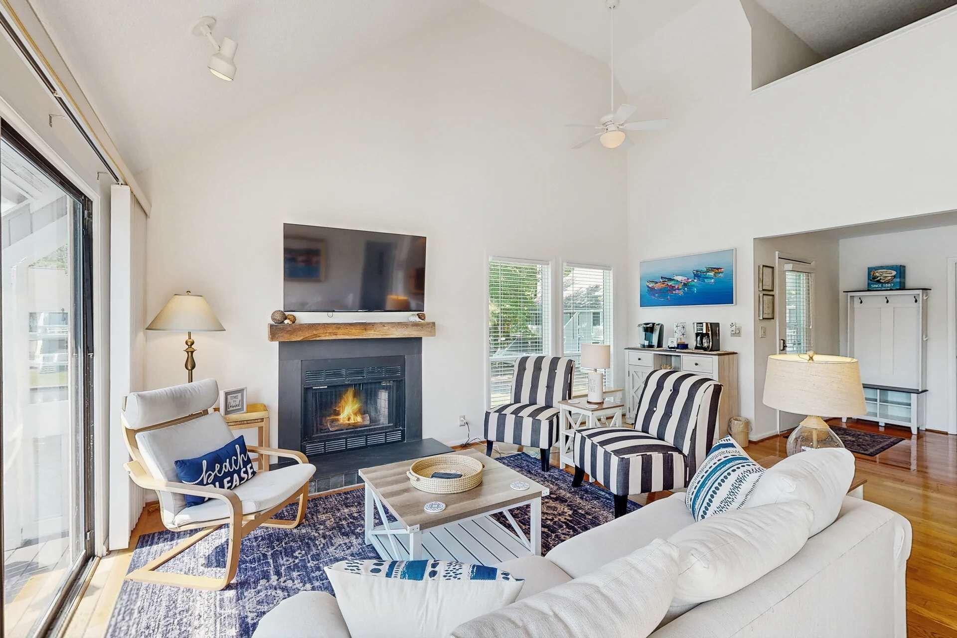 A living room with a fireplace, striped chairs, a white sofa, and a television mounted above the fireplace.