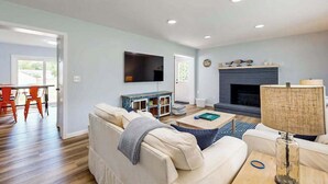 Ein Wohnzimmer mit Sofa, Couchtisch, Fernseher, Kamin und einem Essbereich mit Stühlen.
