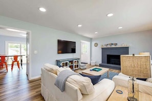 A living room with a sofa, coffee table, TV, fireplace, and a dining area with chairs. - Mill Run Estates home w/free WIFI, W/D, just minutes to the beach (Ocean View)