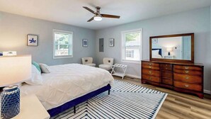 Ein Schlafzimmer mit Bett, Schminktisch, Deckenventilator und Fenstern.