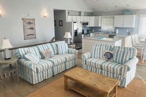 Sala de estar com sofás listrados, uma mesa de centro de madeira e uma cozinha ao fundo.