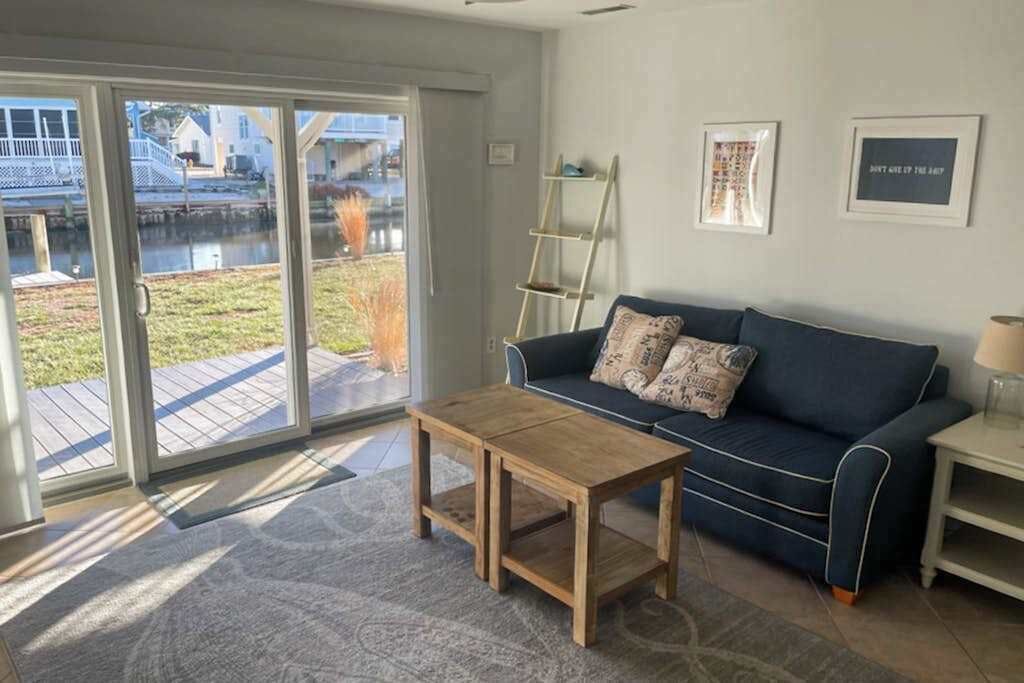 A living room with a sofa, a coffee table, a ladder, and a view through a glass door to an outdoor area.