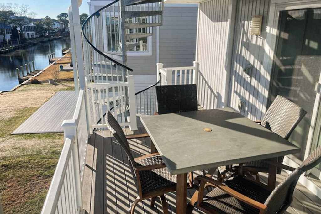 A balcony with a table and chairs, overlooking a body of water and a dock.