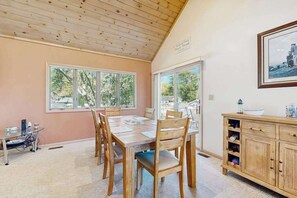 Un coin repas avec une table et des chaises en bois, un buffet en bois et une grande fenêtre donnant sur les arbres.