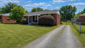 A single-story brick house with a front porch, a gravel driveway, and a fenced yard. - Hibiscus Hideaway | Relaxing 3BR Escape (Columbia)