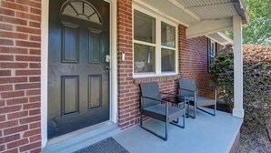 A brick house with a dark front door, a covered porch, and two chairs. - Hibiscus Hideaway | Relaxing 3BR Escape (Columbia)