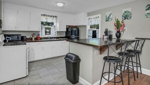 A modern kitchen with white cabinets, a black stove, a coffee maker, and a trash can. - Hibiscus Hideaway | Relaxing 3BR Escape (Columbia)