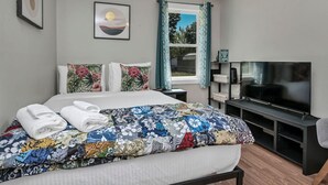 A hotel room with a bed, a TV, a window with curtains, and a bookshelf. - Hibiscus Hideaway | Relaxing 3BR Escape (Columbia)