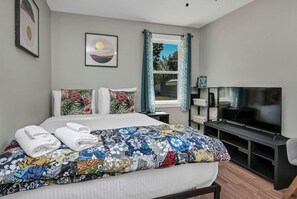 Ein Hotelzimmer mit einem Bett, einem Fernseher, einem Fenster mit Vorhängen und einem Bücherregal.
