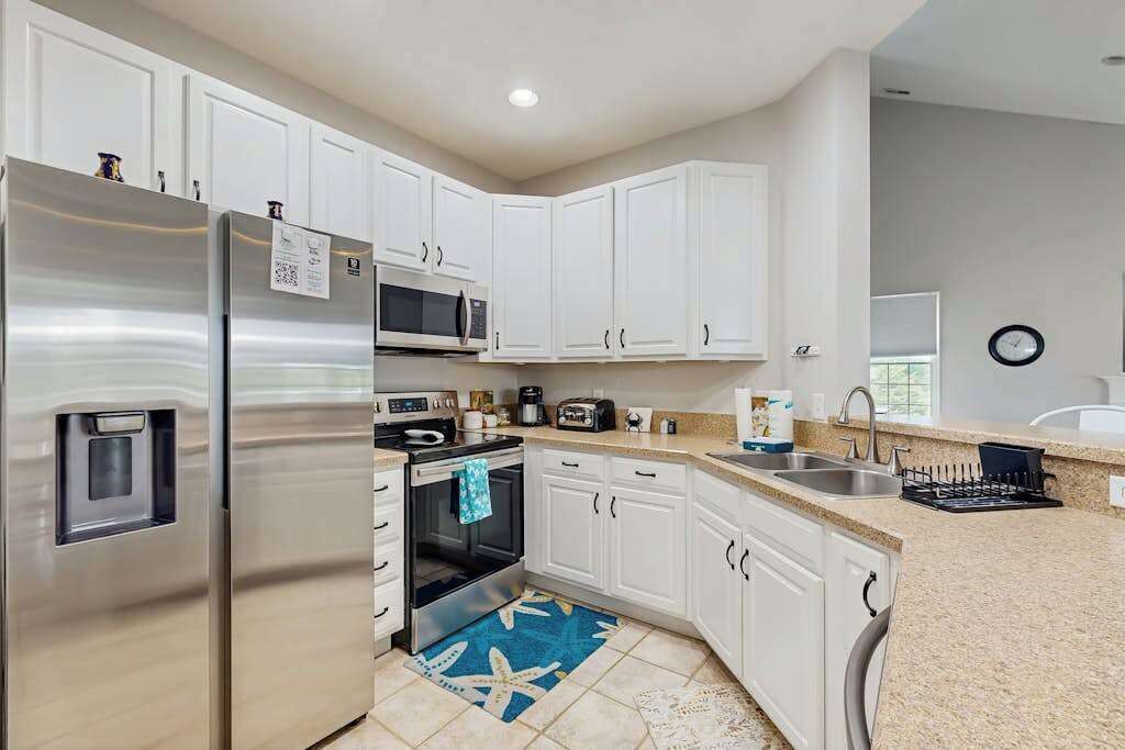 A modern kitchen with white cabinets, stainless steel appliances, a microwave, and a sink.