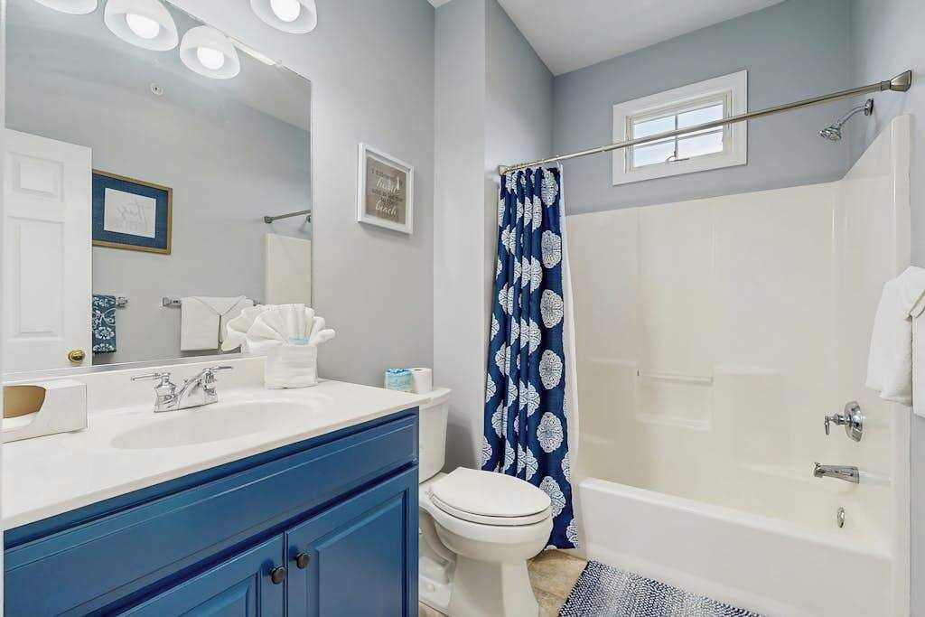 Een badkamer met een witte wastafel, blauwe kastjes, een wit toilet, een douche met een blauw patroonkraam, en een spiegel met verlichting.