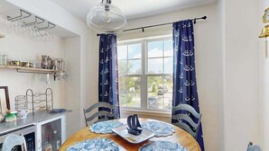 Un coin repas comprenant une table ronde, des chaises, un luminaire suspendu et des rideaux à motifs marins.
