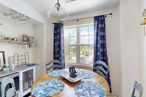 A dining area with a round table, chairs, a hanging light fixture, and curtains with a nautical theme.