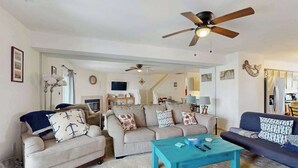 Un salon avec deux canapés, une table basse, des ventilateurs de plafond et un escalier menant à un autre niveau.