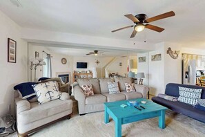 A living room with two sofas, a coffee table, ceiling fans, and a staircase leading to another level.