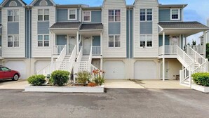 Une rangée de maisons de ville avec des porches à l’avant, un escalier central et une voiture rouge garée dans l’allée.