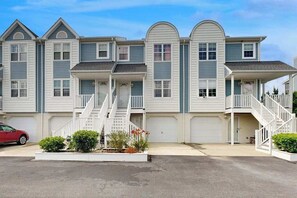 A row of townhouses with front porches, a central staircase, and a red car parked in the driveway.