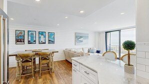 A modern kitchen with wooden flooring, a white countertop, and a dining area with a wooden table and chairs. - Sea Colony 2nd floor oceanside condo w/community pools, tennis, fitness center (Bethany Beach)