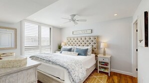 A bedroom with a large bed, a ceiling fan, a bedside table with a lamp, and a window with blinds. - Sea Colony 2nd floor oceanside condo w/community pools, tennis, fitness center (Bethany Beach)