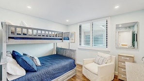 Un dormitorio con una cama litera, una cama individual, una silla, un aparador y una ventana con persianas.