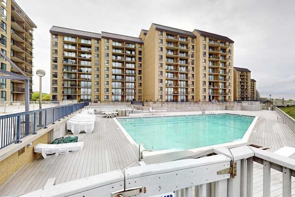 A rooftop swimming pool with a wooden deck, surrounded by high-rise residential buildings.