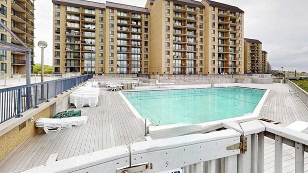 A rooftop swimming pool with a wooden deck, surrounded by high-rise residential buildings. - Sea Colony 2nd floor oceanside condo w/community pools, tennis, fitness center (Bethany Beach)