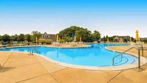 A swimming pool with multiple lanes, surrounded by lounge chairs and umbrellas, with houses and trees in the background. - Bethany Bay house w/community pool, hot tub, tennis, on-site golf (Ocean View)