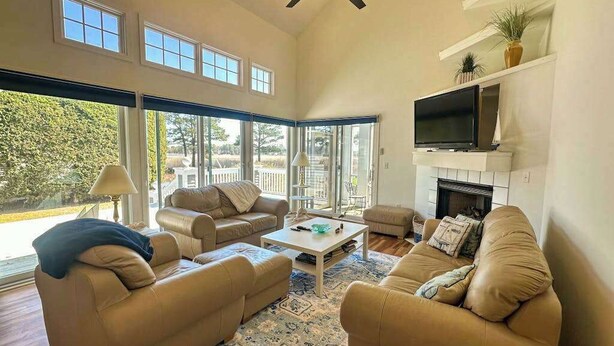 A spacious living room with a fireplace, multiple seating areas, and large windows offering a view of the outdoors. - Bethany Bay house w/community pool, hot tub, tennis, on-site golf (Ocean View)