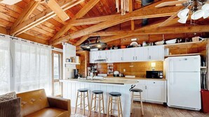 Ein rustikales Blockhaus-Interieur mit Holzbalkendecke, einer Küche mit weißen Schränken, einer Bar und einer gemütlichen Sitzecke.