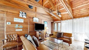 Ein Interieur einer Holzhütte mit einer Couch, einem Fernseher und einem Schild mit der Aufschrift 'SAND SURF'.