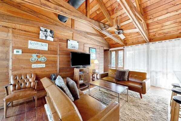 A wooden cabin interior with a sofa, a television, and a sign that reads 'SAND SURF.'