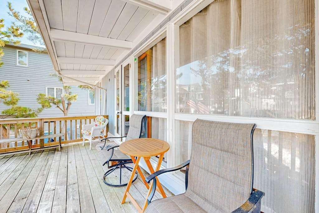 A covered porch with a wooden table and chairs, a bench, and a view of a house.