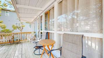 A covered porch with a wooden table and chairs, a bench, and a view of a house.