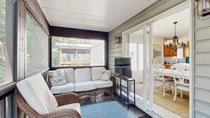 Eine überdachte Veranda mit einer Couch, Korbstühlen, einem Fernseher und einem Essbereich mit weißer Möbel.