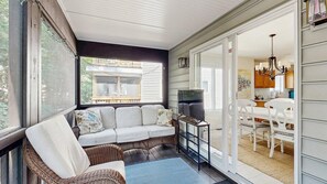 A covered porch with a sofa, wicker chairs, a TV, and a dining area with white furniture. - Town of South Bethany house w/patio, grill, close to beach & restaurants (Bethany Beach)