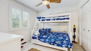 Ein Stockbett mit einer Leiter, ein Schreibtisch und ein Deckenventilator in einem Zimmer mit Fenster und Tür.