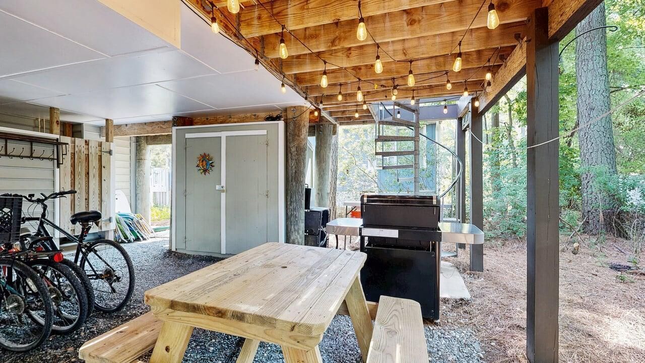 A covered outdoor area with a wooden table and benches, bicycles, and a barbecue grill.
