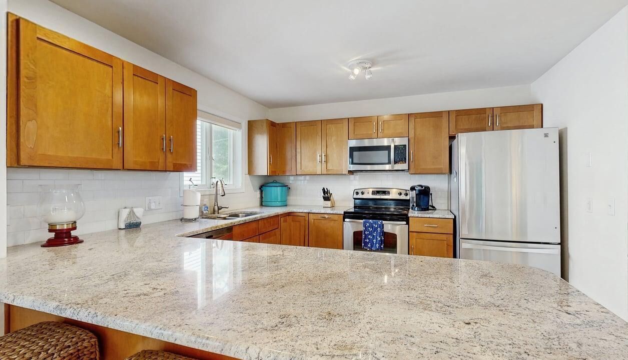 A kitchen with wooden cabinets, a stainless steel refrigerator, a microwave, and a stove.