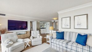 A living room with a sofa, armchairs, a TV, and a dining area with a table and chairs. - Sea Colony 5th floor condo with pools, tennis/pickle ball courts, fitness center (Bethany Beach)