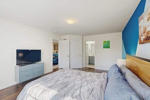 Un dormitorio con cama, televisor, cómoda y puerta que da a un baño.